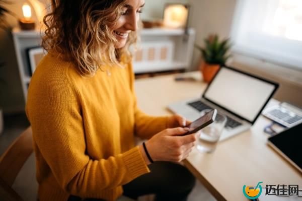 Beautiful young woman sitting at the desk in a home office and using a smart phone.
