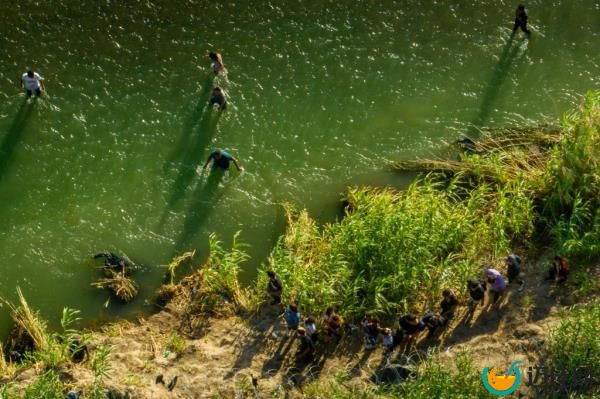 In an aerial view, migrants seeking asylum receive instructions from law enforcement officers after crossing the Rio Grande river into the United States on July 18, 2023 in Eagle Pass, Texas.