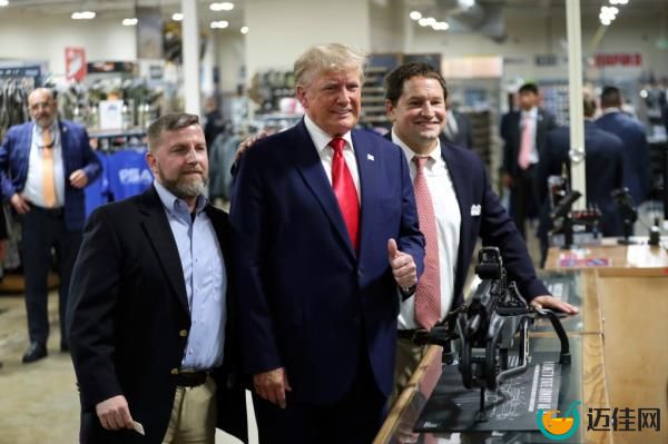 Former President Do<em></em>nald Trump wearing a dark suit white shirt and red tie and giving a thumbs up, visits the Palmetto State Armory and takes a picture with owners Jamin McCallum and Julian Wilson